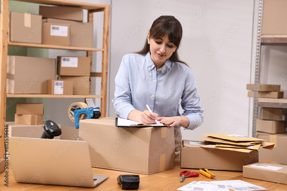 Parcel packing. Post office worker with clipboard writing notes at wooden table indoors Parcel packing. Post office worker with clipboard writing notes at wooden table indoors