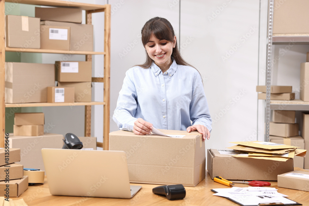 Parcel packing. Post office worker sticking barcode on box at wooden table indoors Parcel packing. Post office worker sticking barcode on box at wooden table indoors