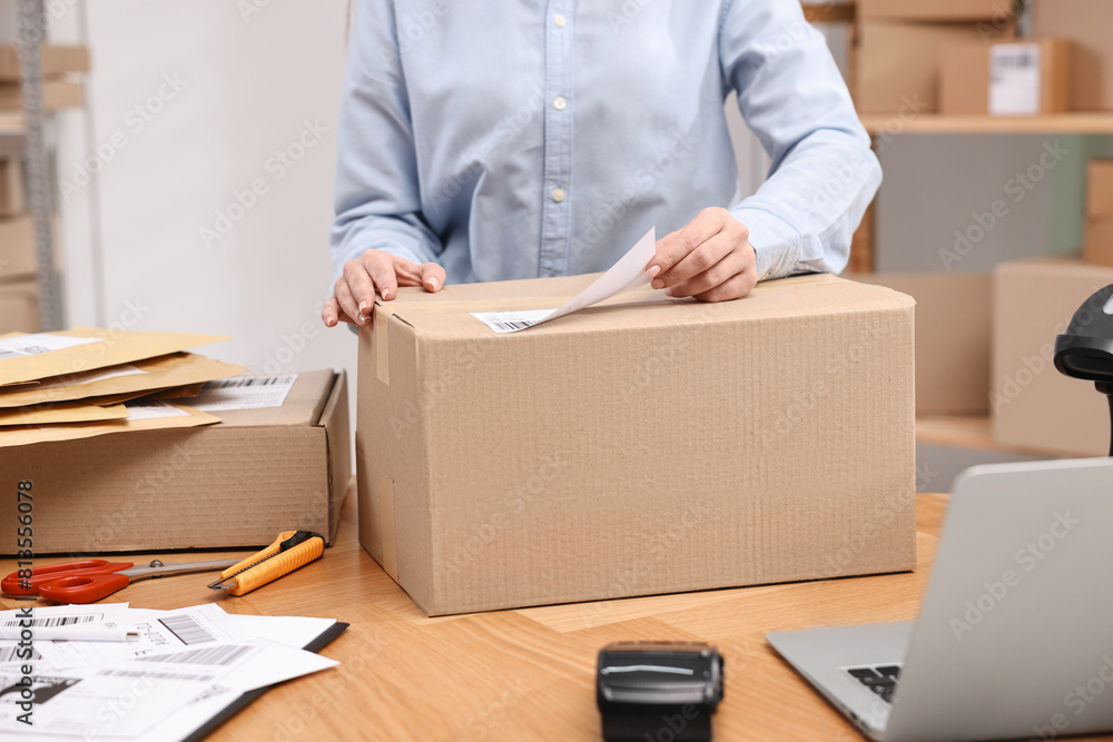 Parcel packing. Post office worker sticking barcode on box at wooden table indoors, closeup Parcel packing. Post office worker sticking barcode on box at wooden table indoors, closeup