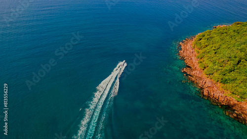 Aerial view of a speedboat cruising along the coast with lush greenery and rocky shoreline, ideal for summer vacation and adventure travel themes