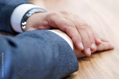 Businessman, politician or official has his hands folded while sitting at a wooden conference table. Clerk, manager, lawyer or deputy. Meeting participant. No face. Photo. Selective focus
