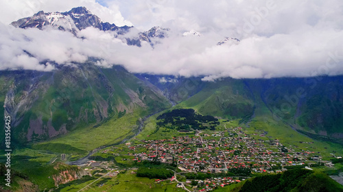 Scenic aerial view of a lush green valley with a village nestled among towering mountains under a cloud-covered sky  ideal for nature and travel themes