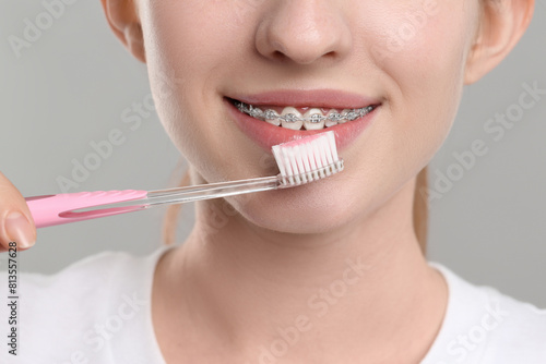 Smiling woman with dental braces cleaning teeth on grey background, closeup