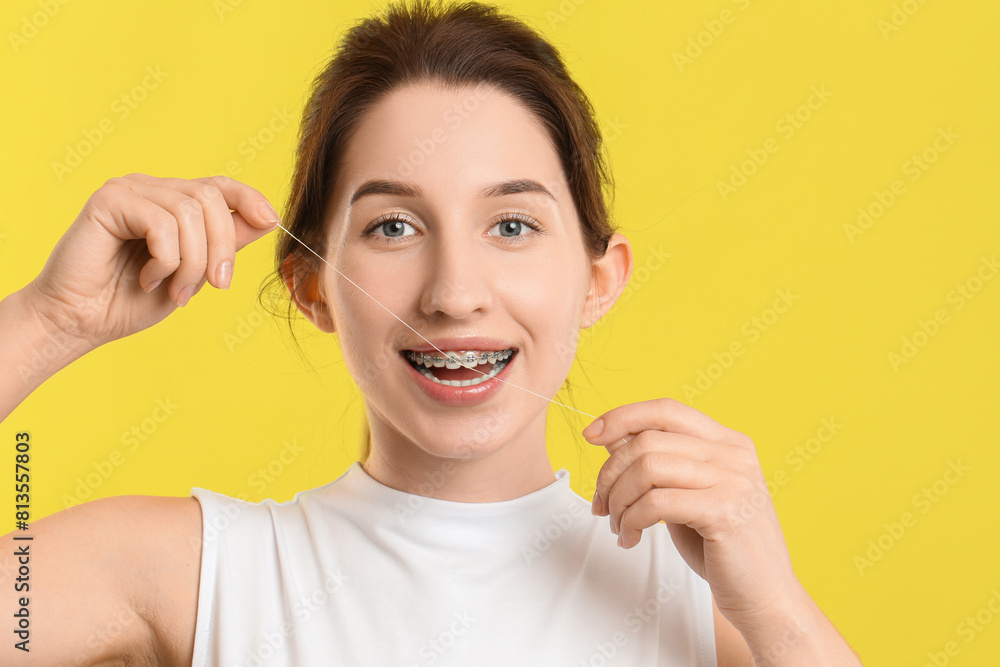 Smiling woman with braces cleaning teeth using dental floss on yellow background Smiling woman with braces cleaning teeth using dental floss on yellow background