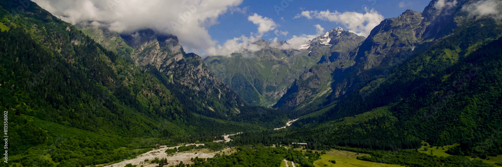 Fototapeta premium Breathtaking panoramic view of vibrant green meadows leading to snow-capped peaks under a blue sky, ideal for nature and travel themes, Earth Day promotions