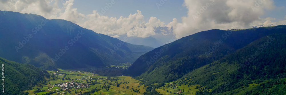 Obraz premium Breathtaking panoramic view of vibrant green meadows leading to snow-capped peaks under a blue sky, ideal for nature and travel themes, Earth Day promotions