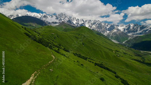 Breathtaking panoramic view of vibrant green meadows leading to snow-capped peaks under a blue sky, ideal for nature and travel themes, Earth Day promotions