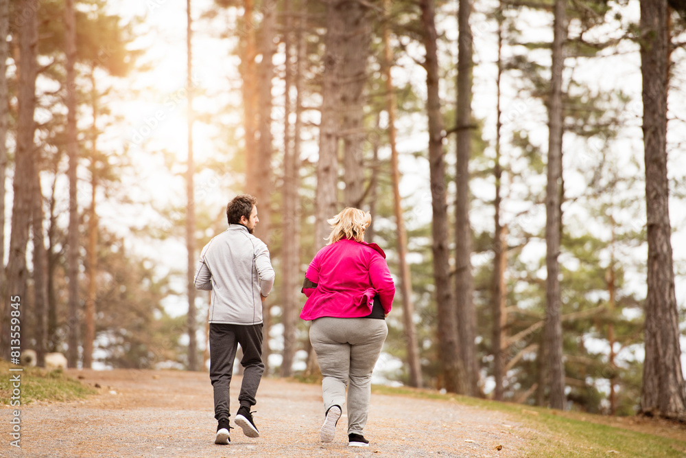 An overweight woman running in nature with friend. Exercising outdoors for people with obesity, support from friend, fitness coach. Rear view. An overweight woman running in nature with friend. Exercising outdoors for people with obesity, support from friend, fitness coach. Rear view.