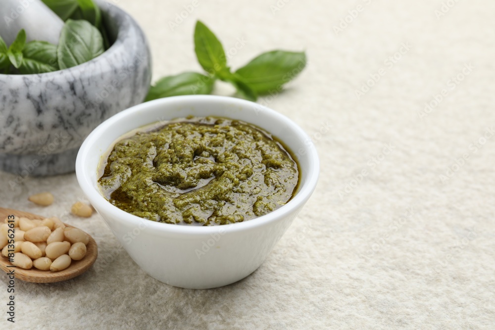 Tasty pesto sauce in bowl, basil, pine nuts and spoon on light grey table, space for text Tasty pesto sauce in bowl, basil, pine nuts and spoon on light grey table, space for text