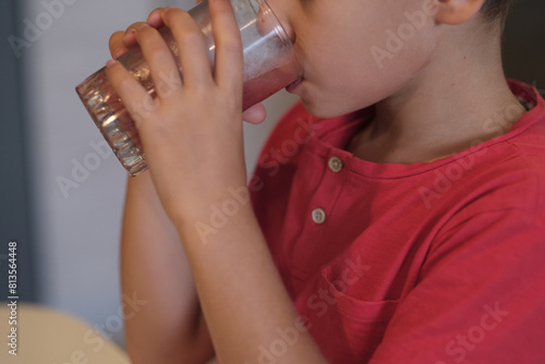 A young boy in a red shirt quenches his thirst with a glass of water, a subtle reminder of the importance of staying hydrated. Perfect for promoting health and hydration.