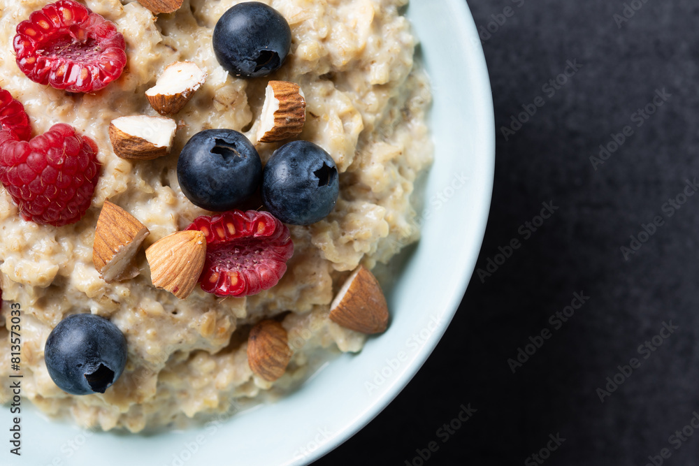 Oatmeal porridge with raspberries, blueberries and almonds in bowl on black background. Close up Oatmeal porridge with raspberries, blueberries and almonds in bowl on black background. Close up