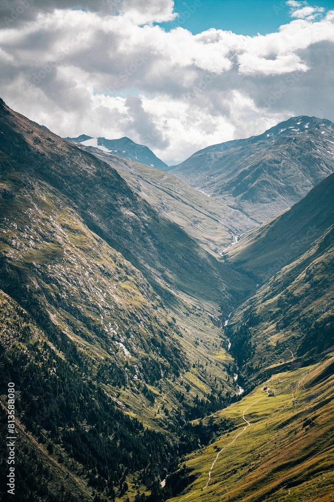 Naklejka premium Vertical high-angle of mountains with valley view sunlit, cloudy sky background