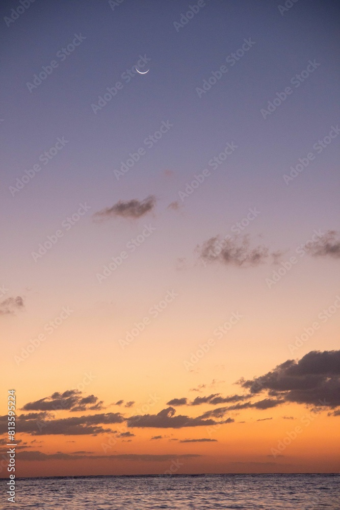 Beautiful view of an ocean during a sunset with dreamy clouds and a waxing crescent moon in the sky Beautiful view of an ocean during a sunset with dreamy clouds and a waxing crescent moon in the sky