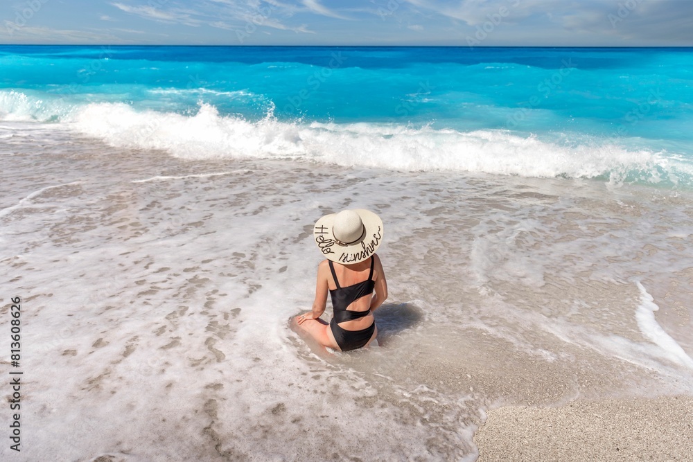 Obraz premium Woman in a big sun hat enjoying the foamy waves of a sea against a blue sky background