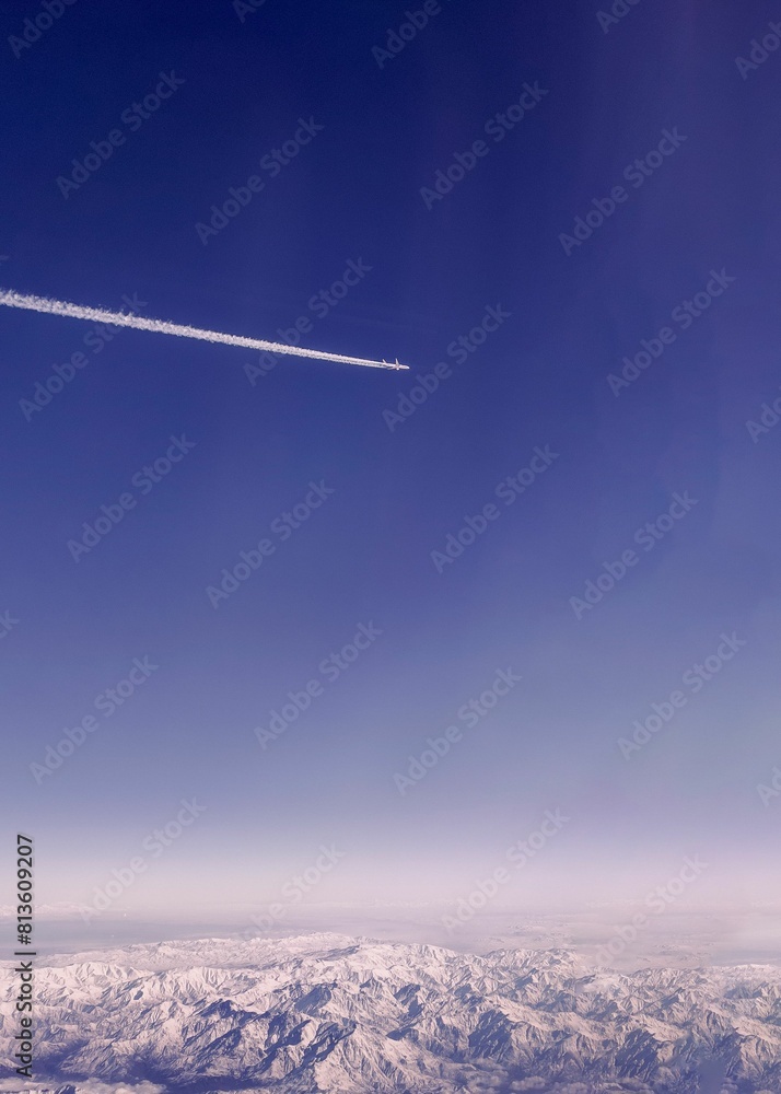 Vertical shot of an airplane flying in the sky over mountains Vertical shot of an airplane flying in the sky over mountains