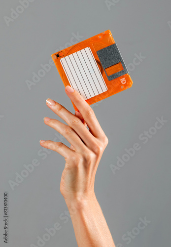 Crop female hand holding orange floppy disk in studio