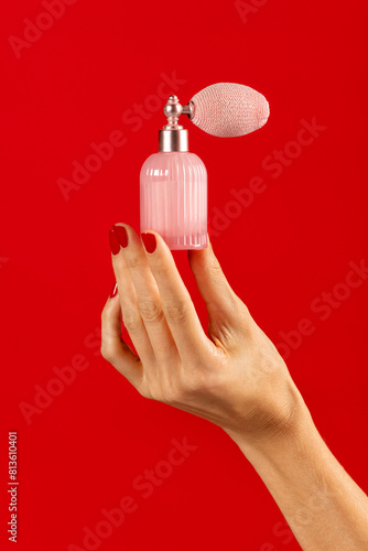 Unrecognizable woman hand holding perfume bottle on red backdrop