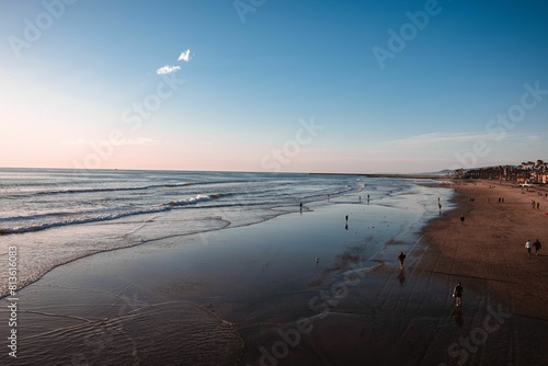 several people are walking and riding their surfboards on the beach photo