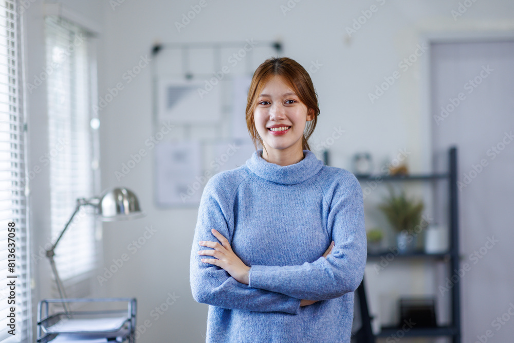 Obraz premium Young Asian business woman smiling confidently while standing alone in a bright modern office