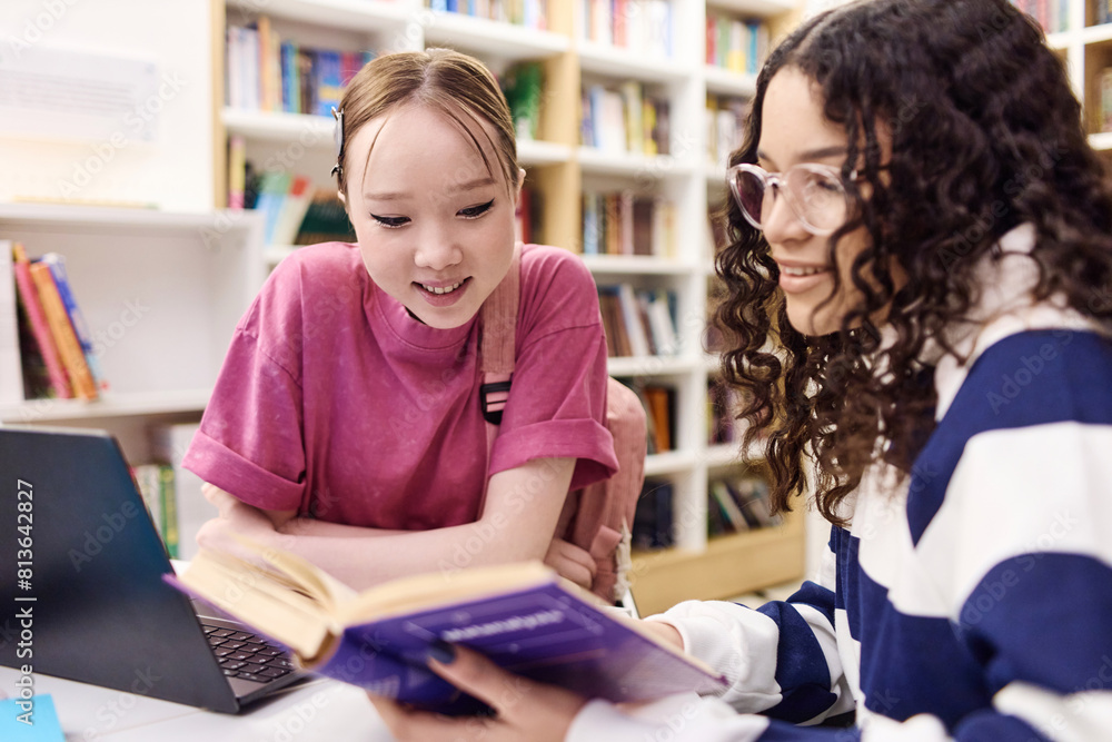 Portrait of two smiling teenage girls in school library studying together and doing homework reading books Portrait of two smiling teenage girls in school library studying together and doing homework reading books
