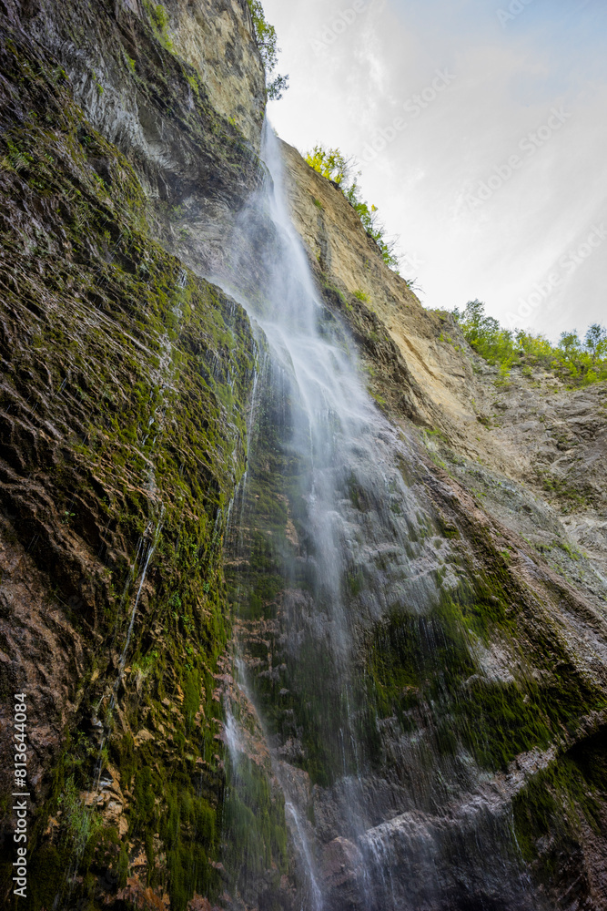 Obraz premium Waterfall hidden inside the forest, beauties of Slovenia to be discovered. Near Nova Gorica, Tolmin village. Water spray and vivid rainbow forms from the waterfall that falls sheer onto the rock.