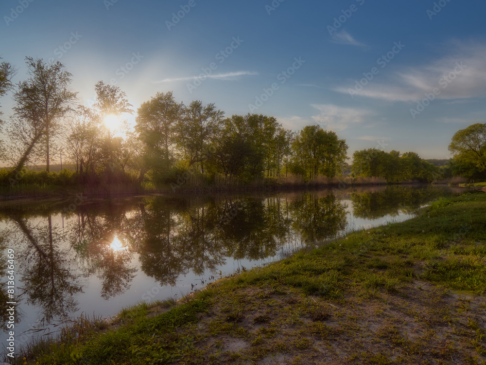 A beautiful sunset on a forest river, the waters of the river flow slowly and the trees and the sun reflect in a mirror, the warm rays of the sun give comfort and magic to this landscape