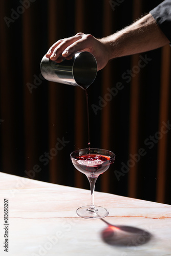 Barman pours cocktail from shaker into glass. Bartender hand pouring fresh alcoholic drink into the glass