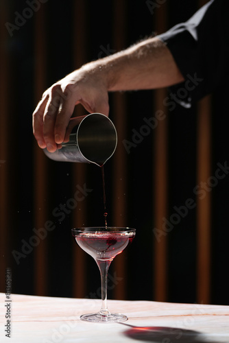 Barman pours cocktail from shaker into glass. Bartender hand pouring fresh alcoholic drink into the glass