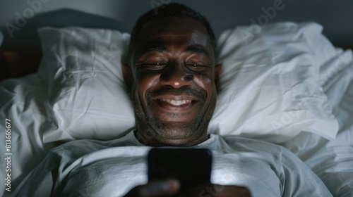 a mature smiling african, american, man lying in bed, looking at his cell phone