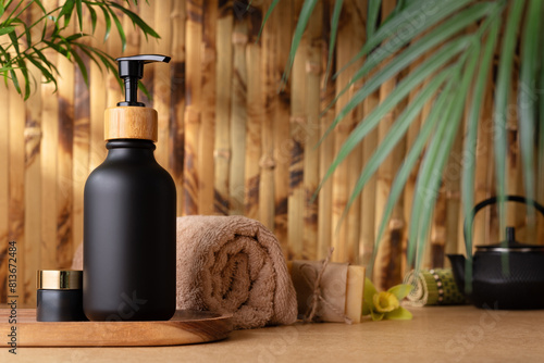 A black pump bottle of lotion or shower gel, sits on a wooden tray against bamboo wall © viktoriya89
