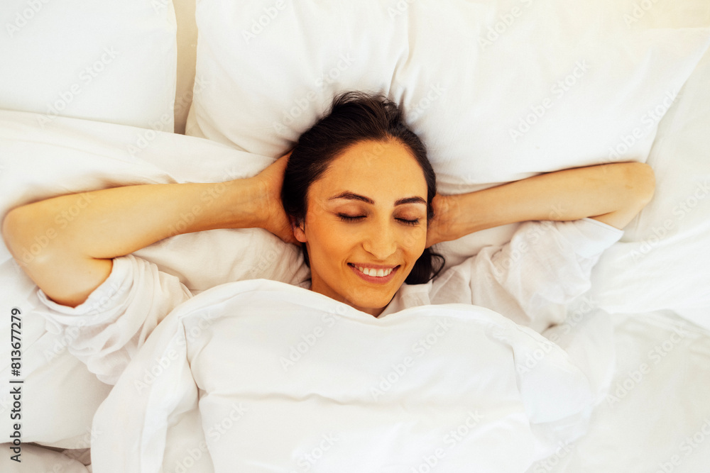 An attractive happy young woman is lying in bed with her eyes closed and her hands behind her head. An attractive happy young woman is lying in bed with her eyes closed and her hands behind her head.
