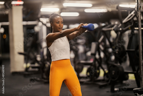 A slim multicultural sportswoman is swinging kettlebell at gym.