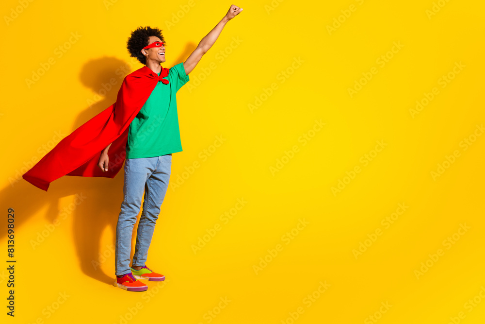 Full length photo of funny super hero costume young man raise fist empty space isolated on yellow color background Full length photo of funny super hero costume young man raise fist empty space isolated on yellow color background