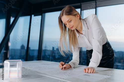the designer contributes to the house project on paper. woman architect designer writes on paper with blueprint. woman in evening office Free Download the designer contributes to the house project on paper. woman architect designer writes on paper with blueprint. woman in evening office - GFXLoad
