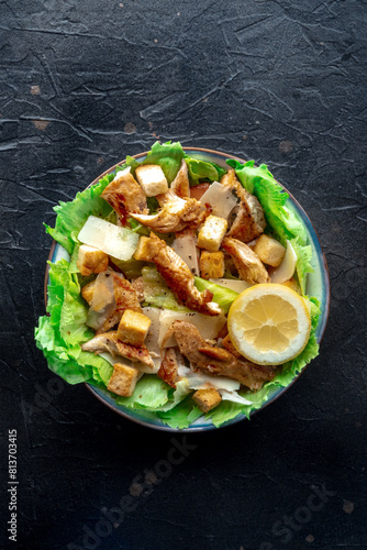 Caesar salad with chicken breast, lettuce, croutons, and a lemon, overhead flat lay shot on a slate background, top view