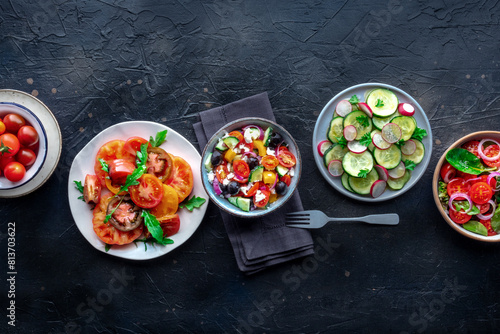 Fresh salads, overhead flat lay shot of an assortment. Variety of plates and bowls with green vegetables. Healthy food on a black slate background