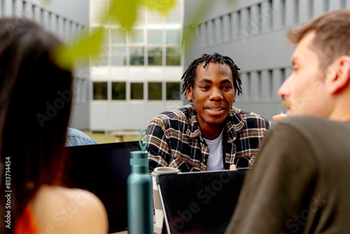 young black male college student chatting with classmates about an academic assignment sitting with laptops outside the campus
