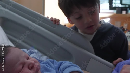 Newborn baby infant being watched by brother at hospital clinic after childbirth, family moment welcoming new member of family photo