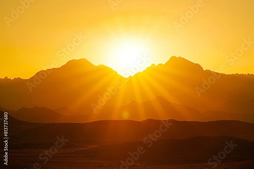 The sun emerges over a desert mountain range  casting a warm golden glow on the landscape
