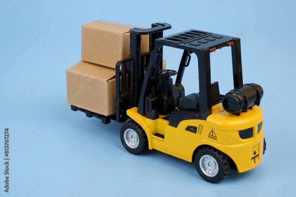 Yellow forklift truck model carrying carton boxes on blue background. Transportation concept.