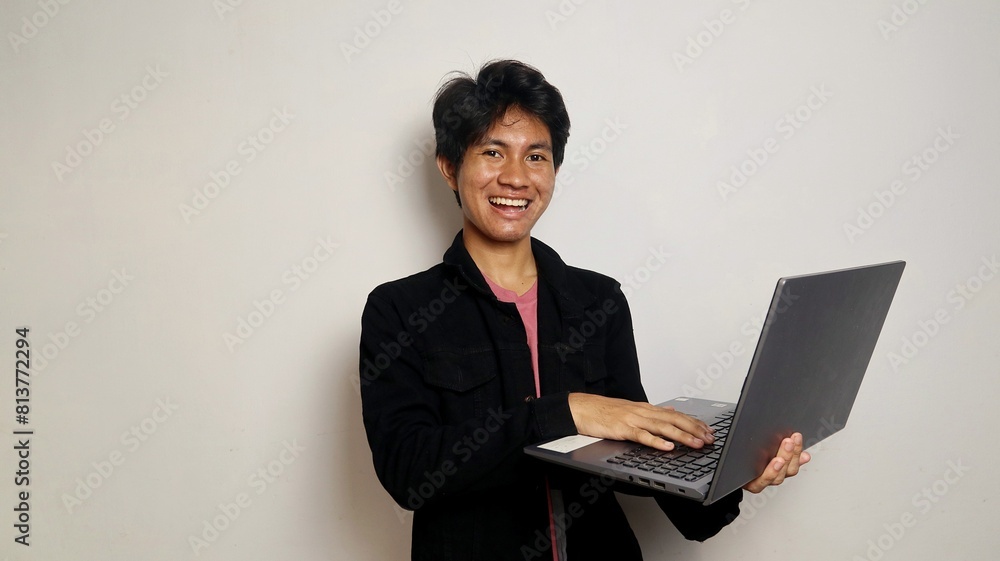 young asian student is standing holding a laptop
