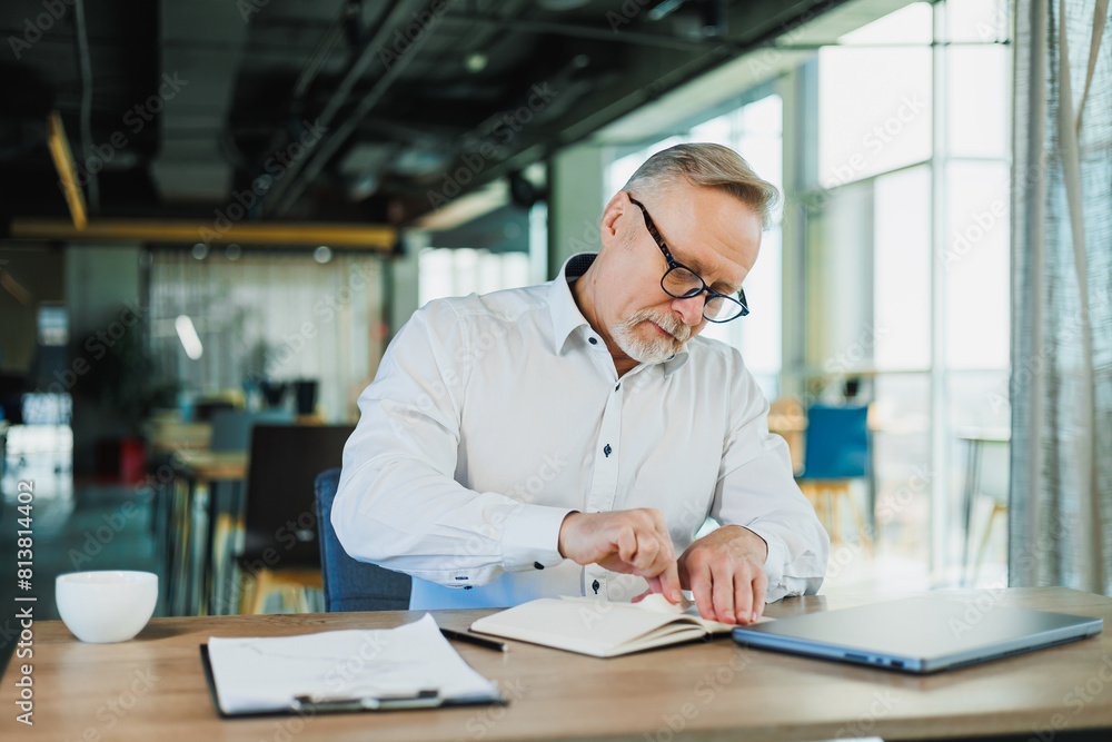 A gray-haired business man in glasses sits at a desk and works with papers. A gray-haired business man in glasses sits at a desk and works with papers.