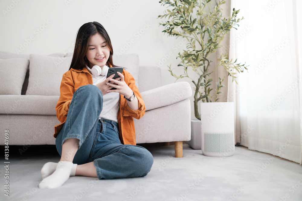 Cheerful young woman with headphone using mobile phone while sitting on floor in living room. Cheerful young woman with headphone using mobile phone while sitting on floor in living room.
