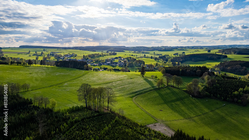 This aerial photograph captures the vast and verdant landscape of the Hautes Fagnes region  characterized by its rolling hills and vibrant green fields. The image showcases the area s natural beauty