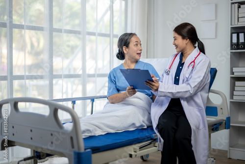 A woman in a white coat is talking to an older woman in a hospital bed