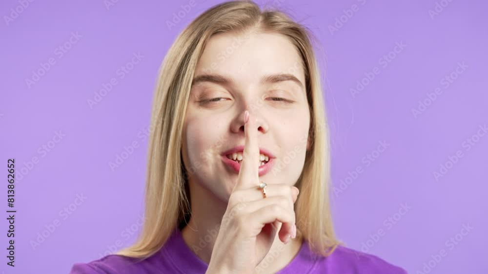 Smiling cheerful woman with finger on lips - shh, secret, silence,violet studio Smiling cheerful woman with finger on lips - shh, secret, silence,violet studio