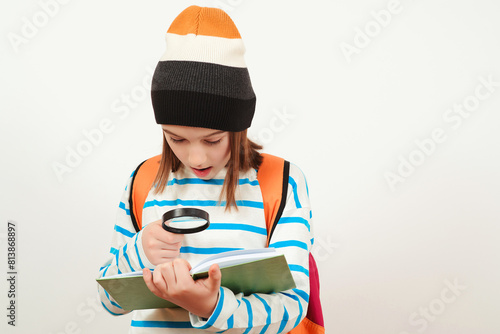 Boy looking through magnifying glass to the book. Schoolboy holding the magnifying glass. Children's interest. Portrait of student boy with magnifier.