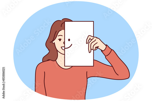 Happy woman covers half of face with paper with smiling emoticon, wanting to share good mood and positive with people around. Kind girl carelessly looks at camera enjoying life and enjoying moment