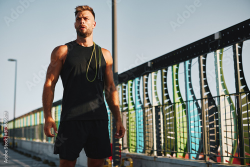 Handsome sports man posing with jump rope on his shoulder after training in black sports clothes