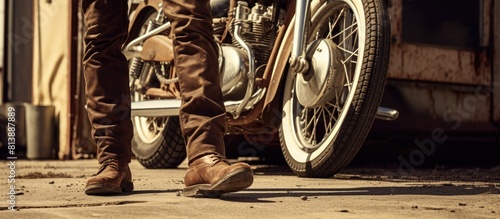A person wearing vintage brown quadrille pants and brown sneakers stands next to an old motorcycle showing their legs and feet in the copy space image photo